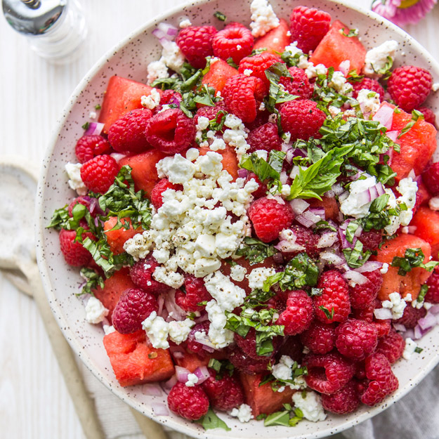 Watermelon and raspberry salad with feta and basil on a speckled plate.