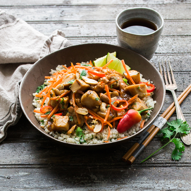Stir-fry chicken and vegetables over rice in a bowl with chopsticks, rustic wooden table.