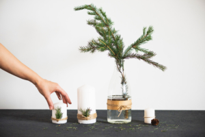 Hand reaching for a candle beside a vase with a pine branch on a black table, white background. Hand reaching for a candle beside a vase with a pine branch on a black table, white background.