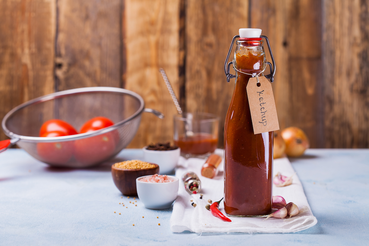 Homemade ketchup in a bottle with spices and tomatoes on a rustic wooden background.