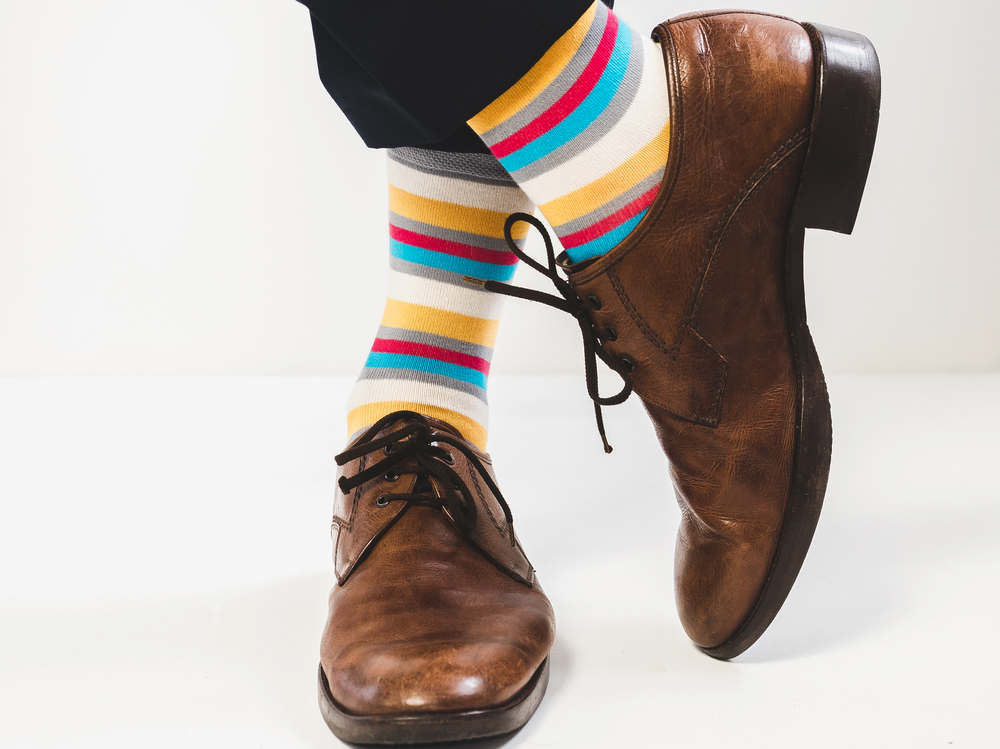 Person in brown shoes and colorful striped socks against a white backdrop.