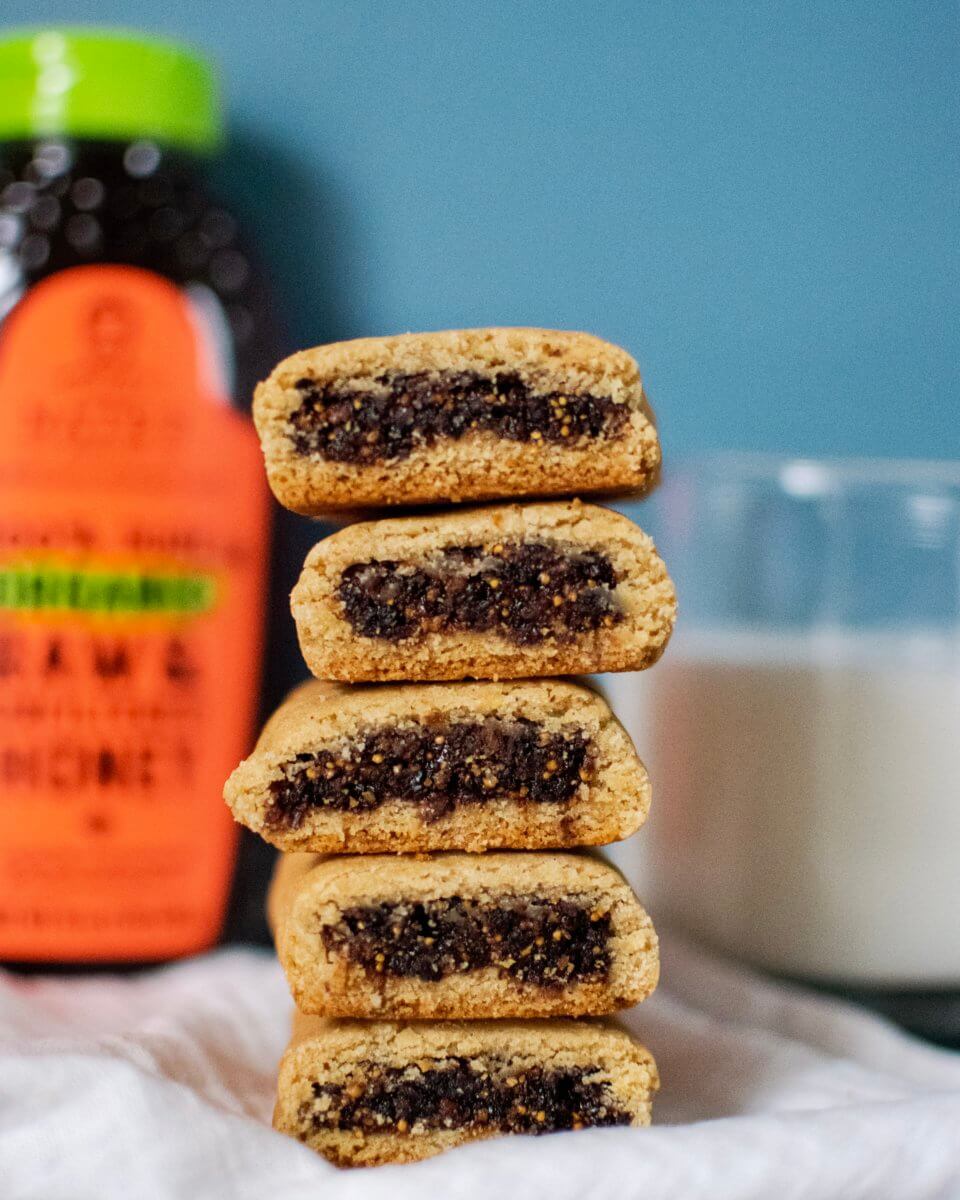 Stacked homemade fig cookies made with honey with a Nate’s organic honey bottle and a glass of milk in the background.