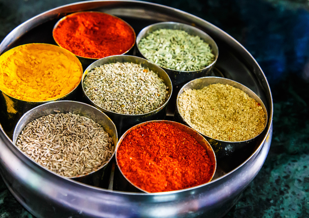 Assorted colorful spices in a round container on a marbled surface.