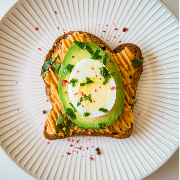 Hummus, avocado and egg toast with red pepper flakes and parsley on a white striped plate.