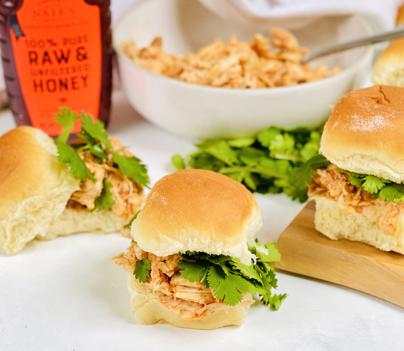 Chicken sliders with cilantro on a board, Nate's raw honey bottle in the back.