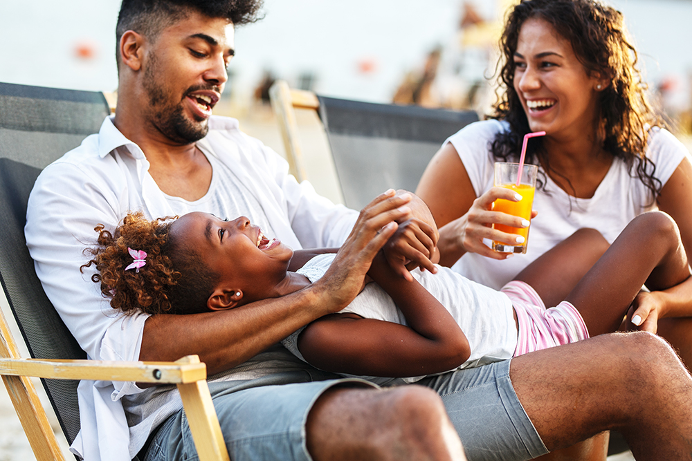 Family enjoying time together on beach chairs with drinks.
