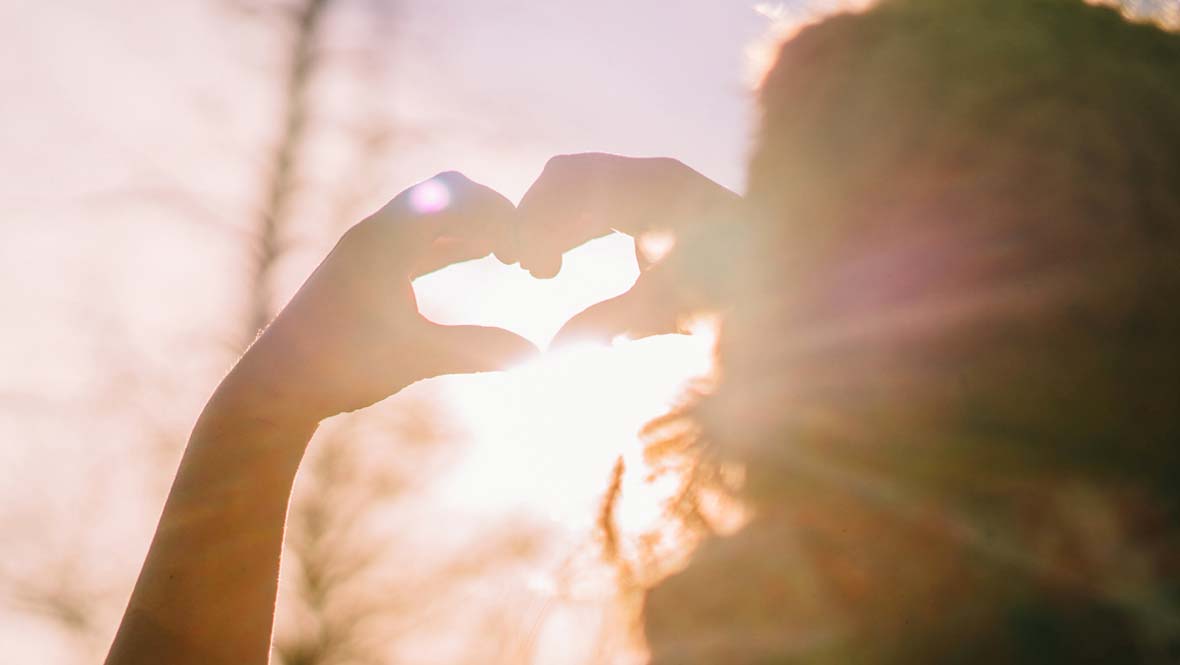 Silhouette of hands forming a heart shape with the sun shining through.