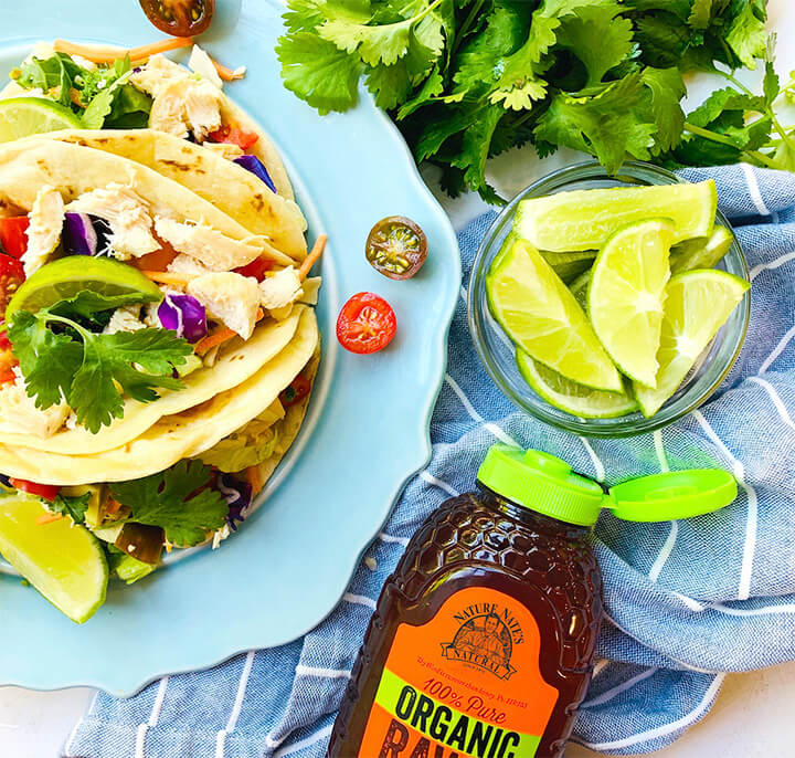 Nate's organic honey bottle with tacos, lime slices on a blue napkin, and fresh cilantro.