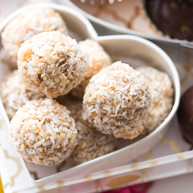Coconut-covered energy bites in a white heart-shaped container, close-up view.