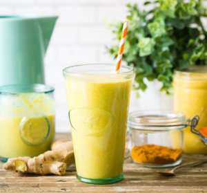 A refreshing turmeric and ginger smoothie in a glass with a straw, alongside ingredients on a rustic wooden table.