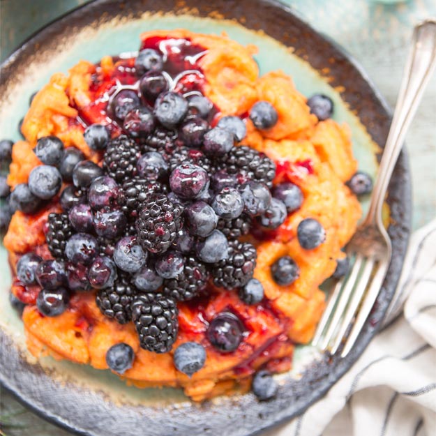 Sweet potato waffles topped with blueberries and blackberries in a rustic bowl.