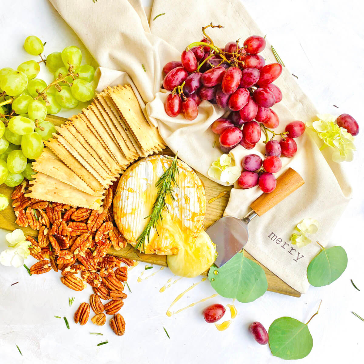 A vibrant cheese platter with grapes, crackers, nuts and brie drizzled with honey arranged on a beige cloth.