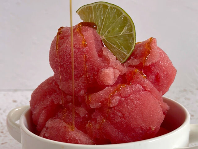 Round scoops of pink watermelon sorbet on top of each other. Topped with a lime slice and drizzled with honey.