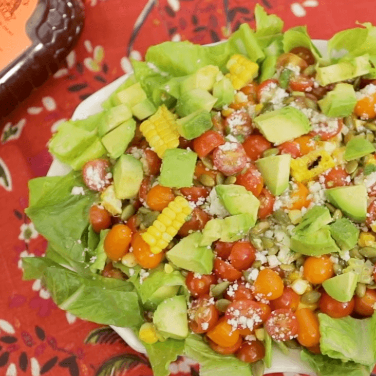 Colorful salad with corn, tomatoes, avocado and cheese on a red patterned cloth.