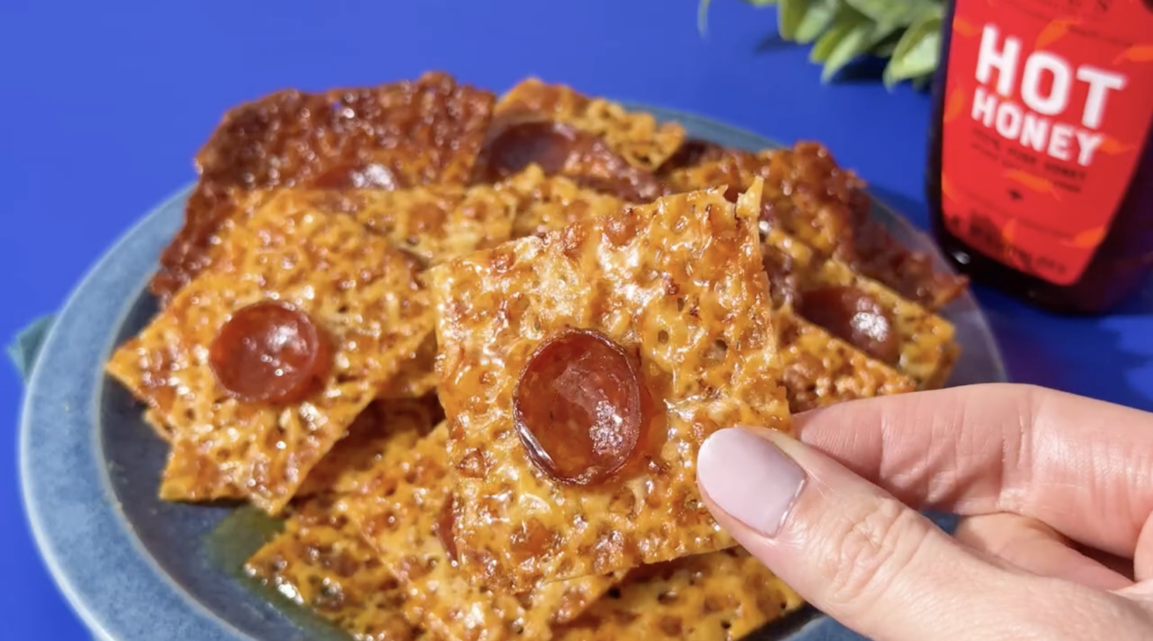 Cheesy Pepperoni Chips in hand with Nate's hot honey in the background.