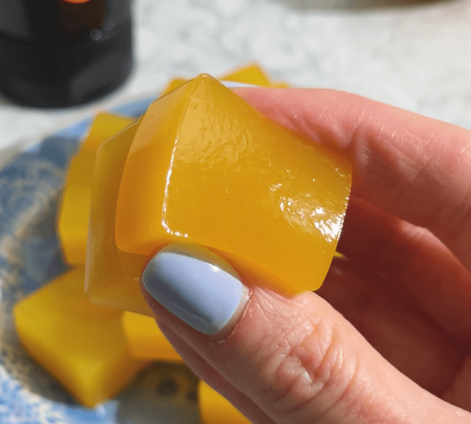 Hand holding a yellow jelly cube over a plate of more cubes.