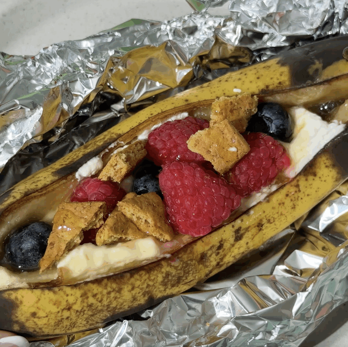 Baked Banana Boat in foil topped with raspberries, blueberries, and honey.