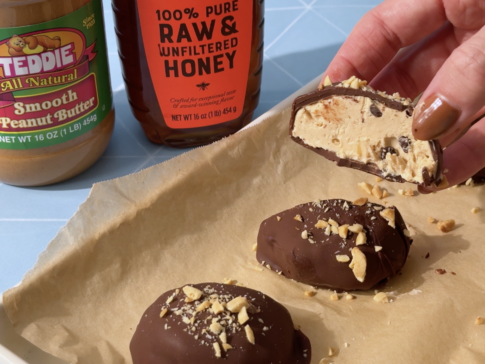 Chocolate-coated honey yogurt peanut butter bites on parchment paper with bottles of honey and peanut butter in background.